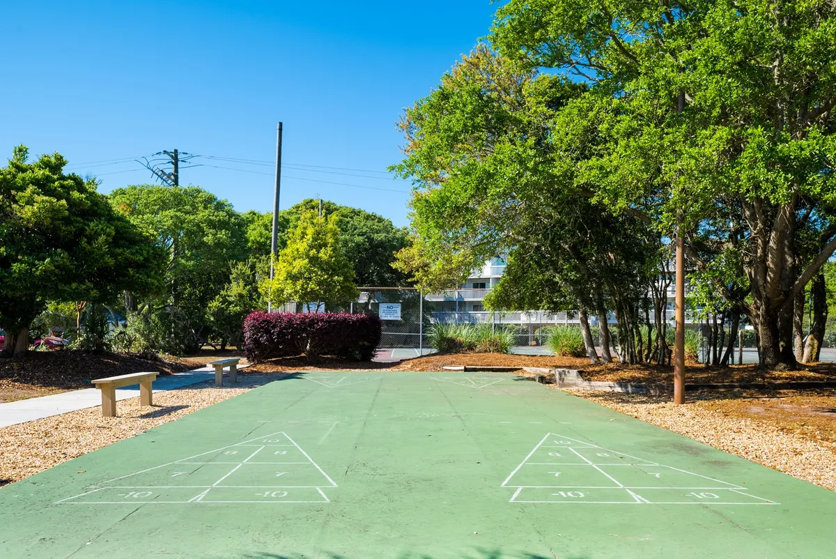 A shuffleboard court bordered by lush greenery and benches, inviting families to play and relax together. The bright outdoor setting emphasizes active recreation and social interaction in a safe environment.