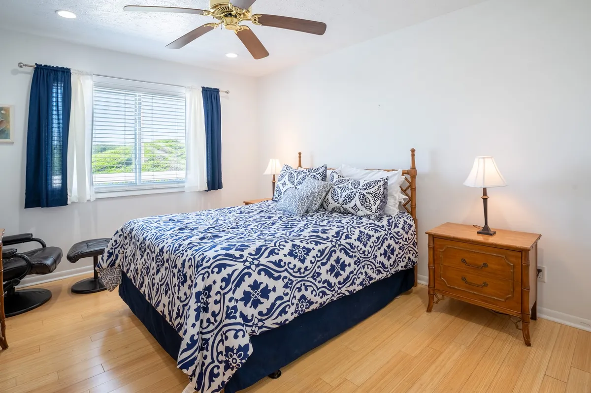 A tranquil bedroom featuring a neatly made bed with patterned bedding, soft natural light flooding in through the window, and a nightstand topped with a lamp. The room exudes a calming atmosphere, suggesting a restful retreat after a day by the sea.