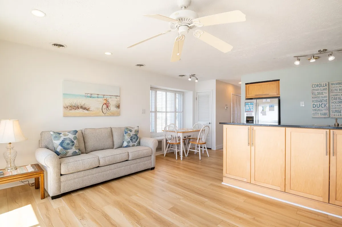 An inviting space with a sofa, dining table, kitchen countertop, and decorative wall art, all bathed in gentle morning light. The arrangement is casual yet comfortable, encouraging relaxation, dining, and time together.