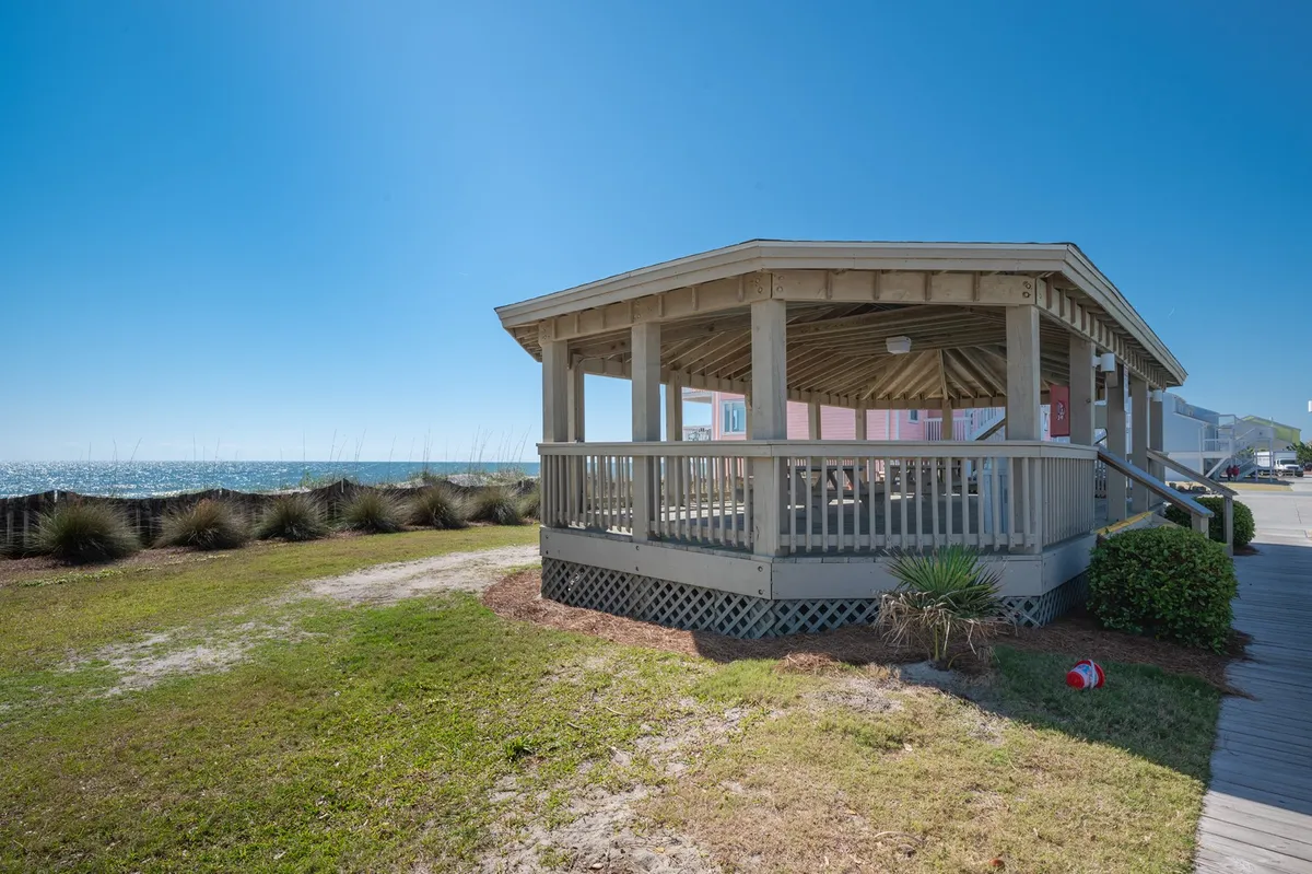 A tranquil pavilion structure set on green grass with the ocean in the background. The setting is ideal for picnicking, relaxing with a partner, or gathering before heading out to explore local parks, historic sites, or take scenic ferry rides.