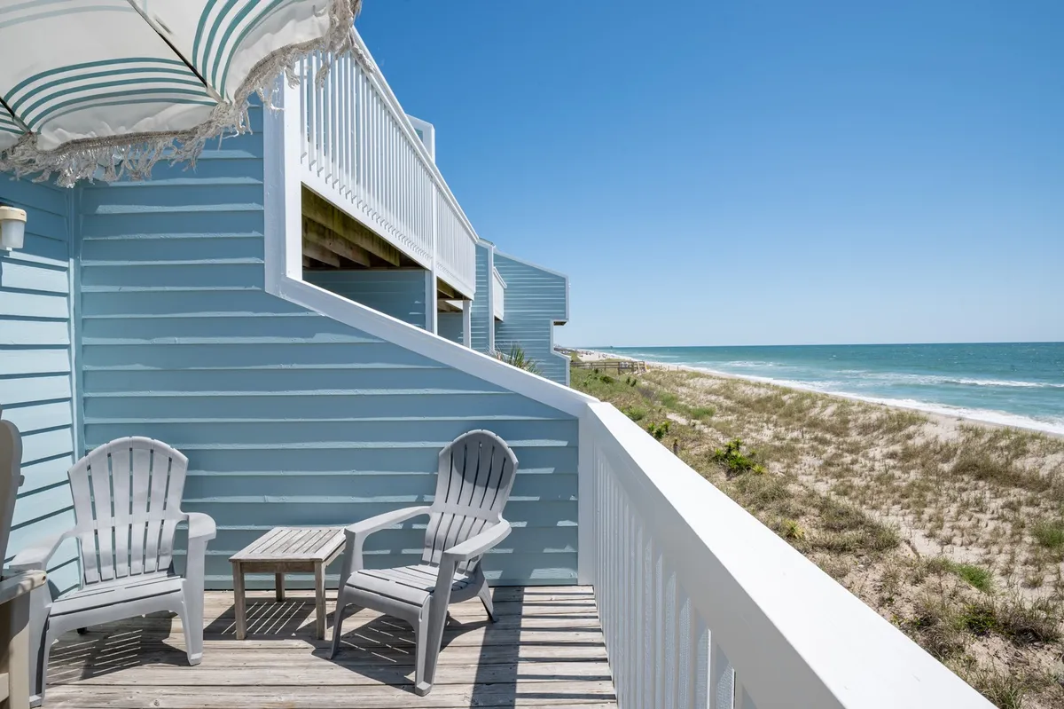 A private balcony with Adirondack chairs and a small table overlooks the beach and ocean. The tranquil setting invites guests to enjoy coffee at sunrise, relax with a book, or watch the sunset while listening to the waves.
