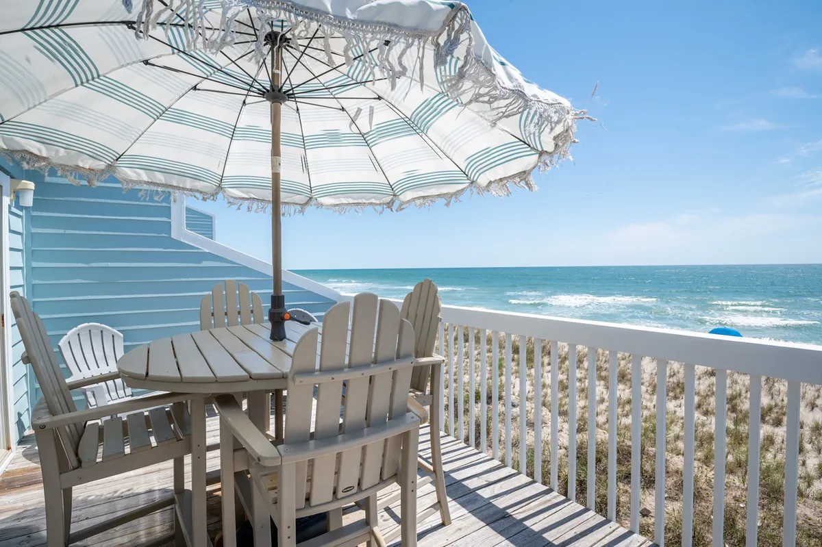 The image showcases a private outdoor dining space with a table and umbrella overlooking the sparkling Atlantic, capturing an inviting beachfront setting. The tranquil ocean view, ample sunlight, and cozy deck present perfect spots for al fresco meals, sunbathing, or simply relaxing by the sea.